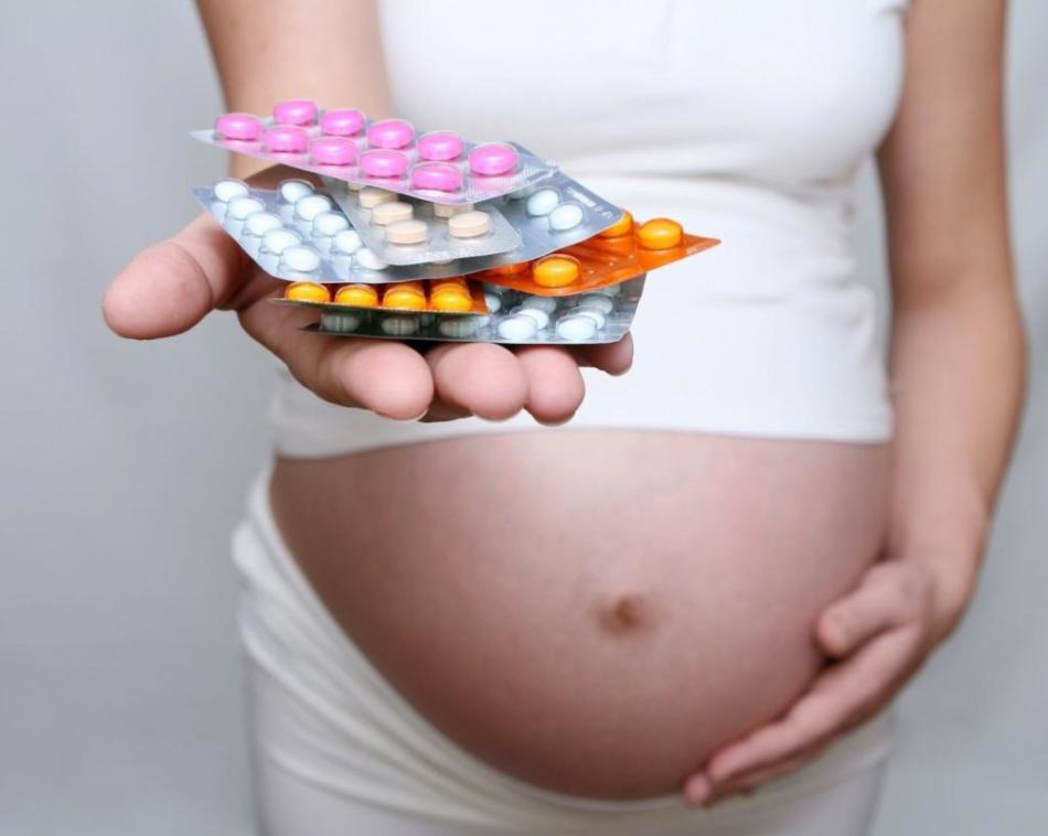 Беременная девушка держит на ладошке горсть антидепрессантов в блистерах