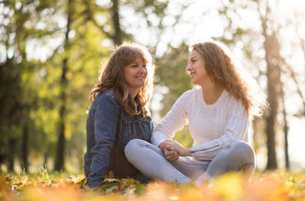 Мама общается со взрослой дочерью, сидя на осенней листве